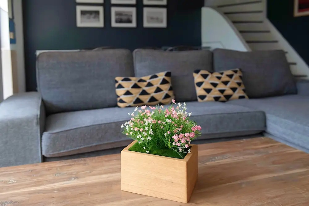 Urne Marguerite Rose en hêtre avec fleurs artificielles, dans un salon.
